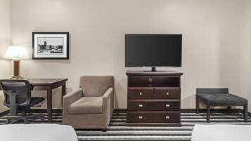 Una habitación de hotel con cama, escritorio, silla, cómoda, televisor y un cuadro en la pared.