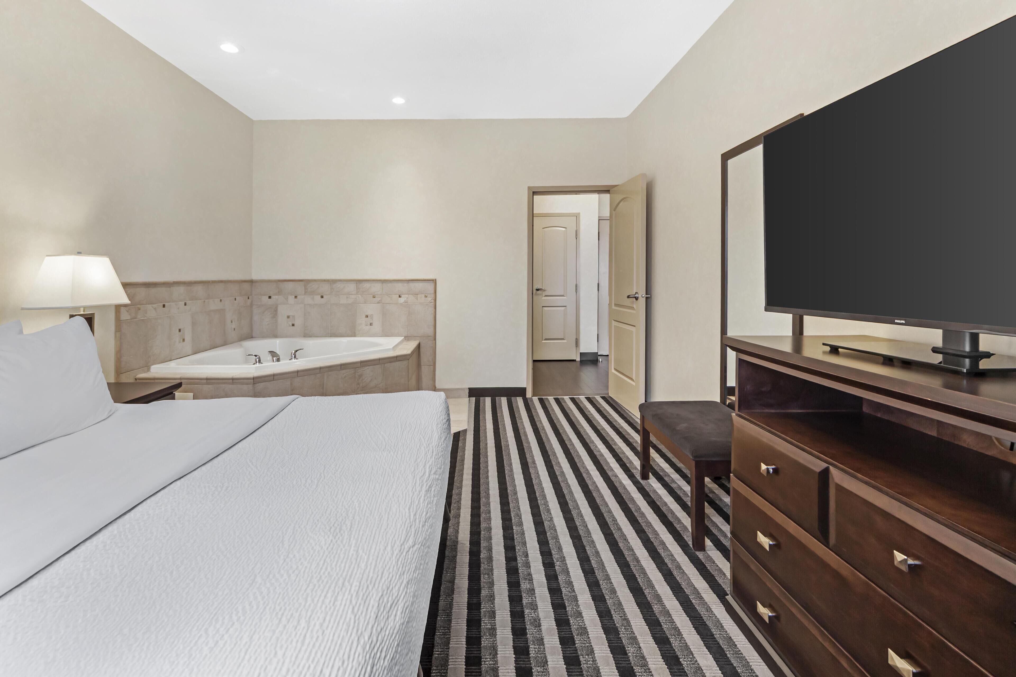 A hotel room with a bed, a TV, a desk, a chair, a lamp, and a bathroom with a bathtub and shower.