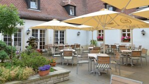 An outdoor patio with tables and chairs, yellow umbrellas, and potted plants. - Churfuerstliche Waldschaenke Moritzburg (Moritzburg)