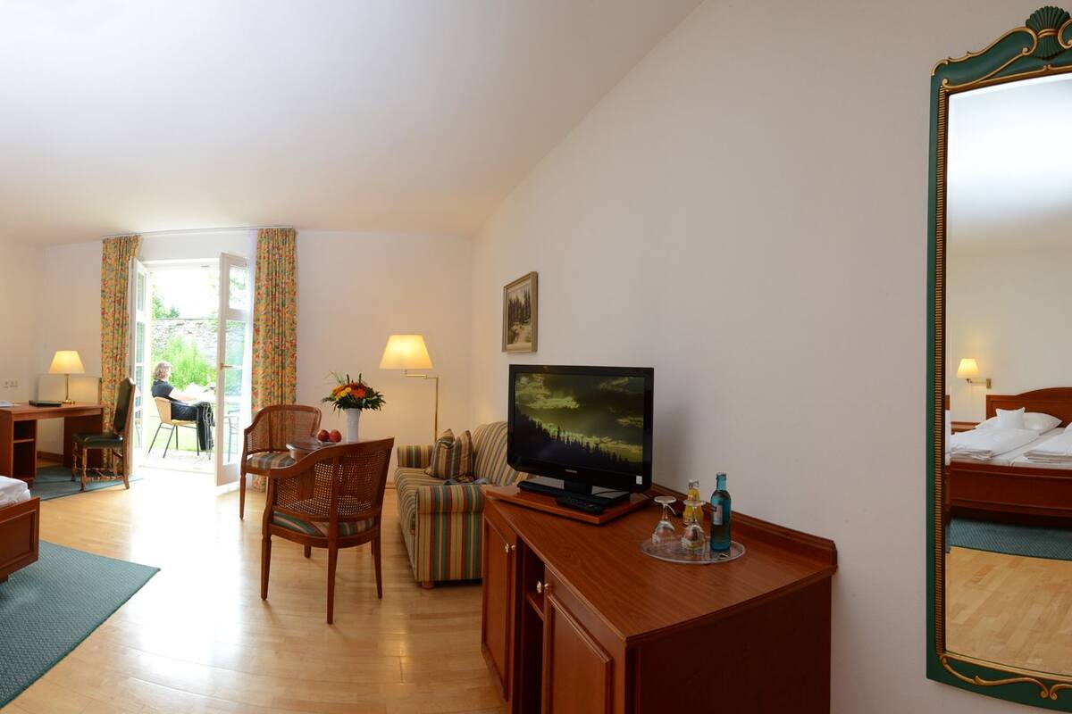 A hotel room with a large bed, a desk, a chair, a television, and a mirror.