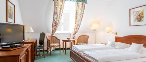 Een hotelkamer met een bed, twee stoelen, een bureau met een televisie en een raam met gordijnen.