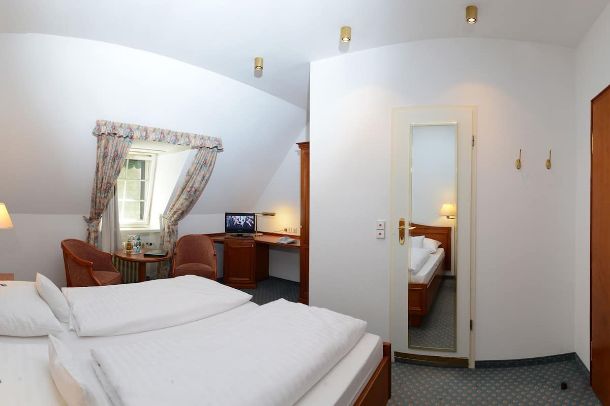 A hotel room with two beds, a desk with a computer, a chair, a lamp, and a window with curtains.