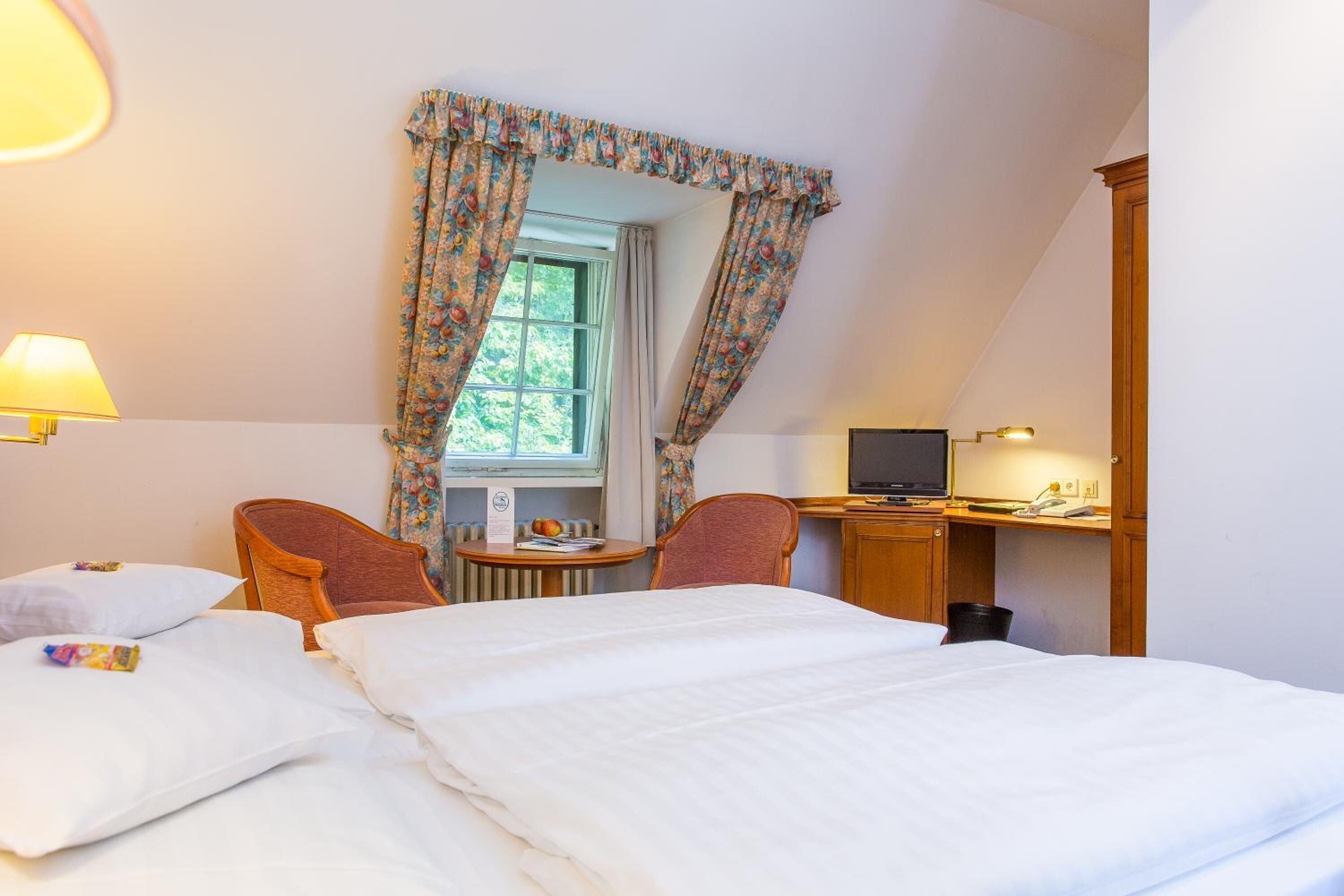 Habitación de hotel con dos camas, un escritorio con computadora y una ventana con cortinas.