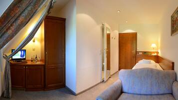 A hotel room with a bed, a desk with a computer, a chair, and a bathroom door.