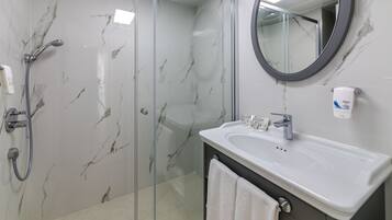 A modern bathroom with a glass-enclosed shower, a white sink with a Dove soap dispenser, and a round mirror.