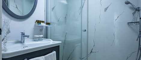 Un baño moderno con ducha envuelta en vidrio, pared con azulejos de mármol, lavamanos blanco con espejo y tocador oscuro.
