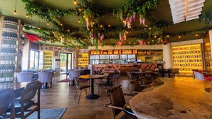 Un interior de restaurante con mesas y sillas de madera, una zona de bar y estanterías con botellas.