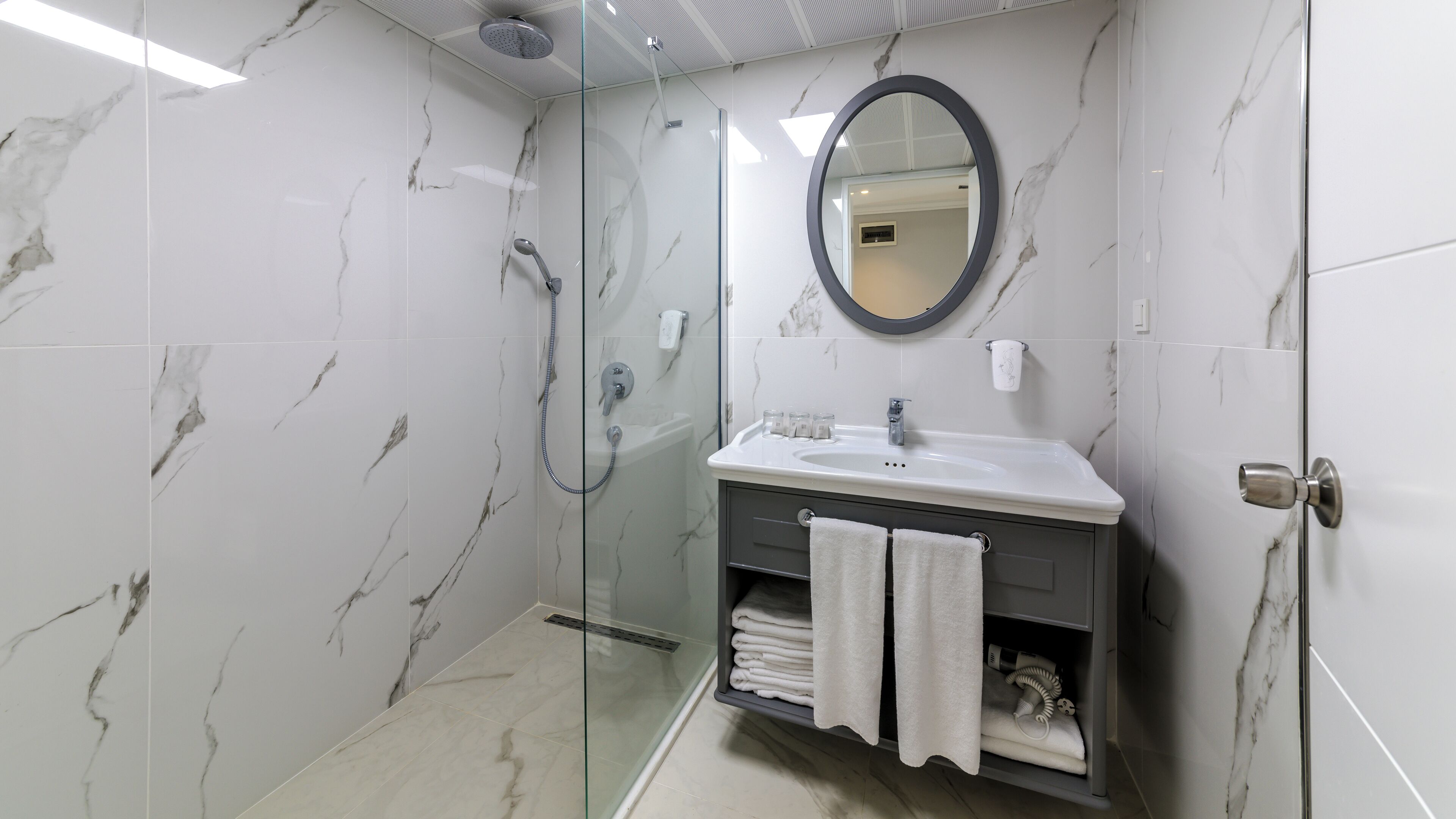 Un baño moderno con ducha envuelta en vidrio, tocador con lavamanos y espejo.