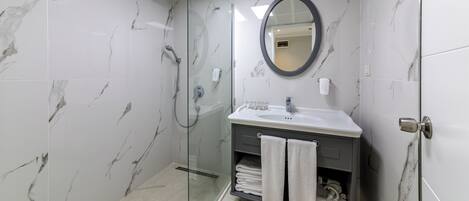Un baño moderno con ducha envuelta en vidrio, tocador con lavamanos y espejo.
