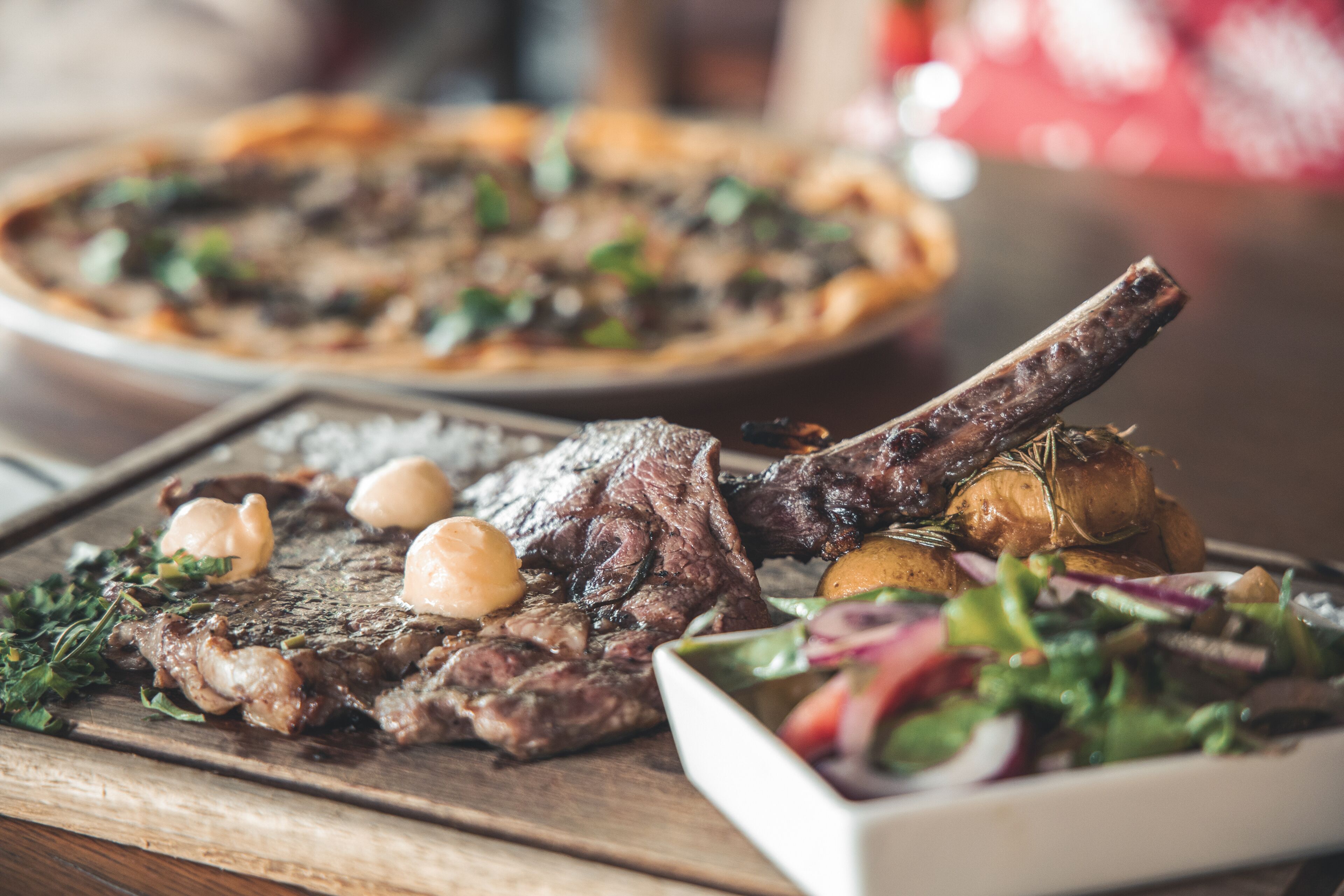 Ein Steak mit Knochen, serviert mit Salat und Bratkartoffeln auf einem Holztisch.