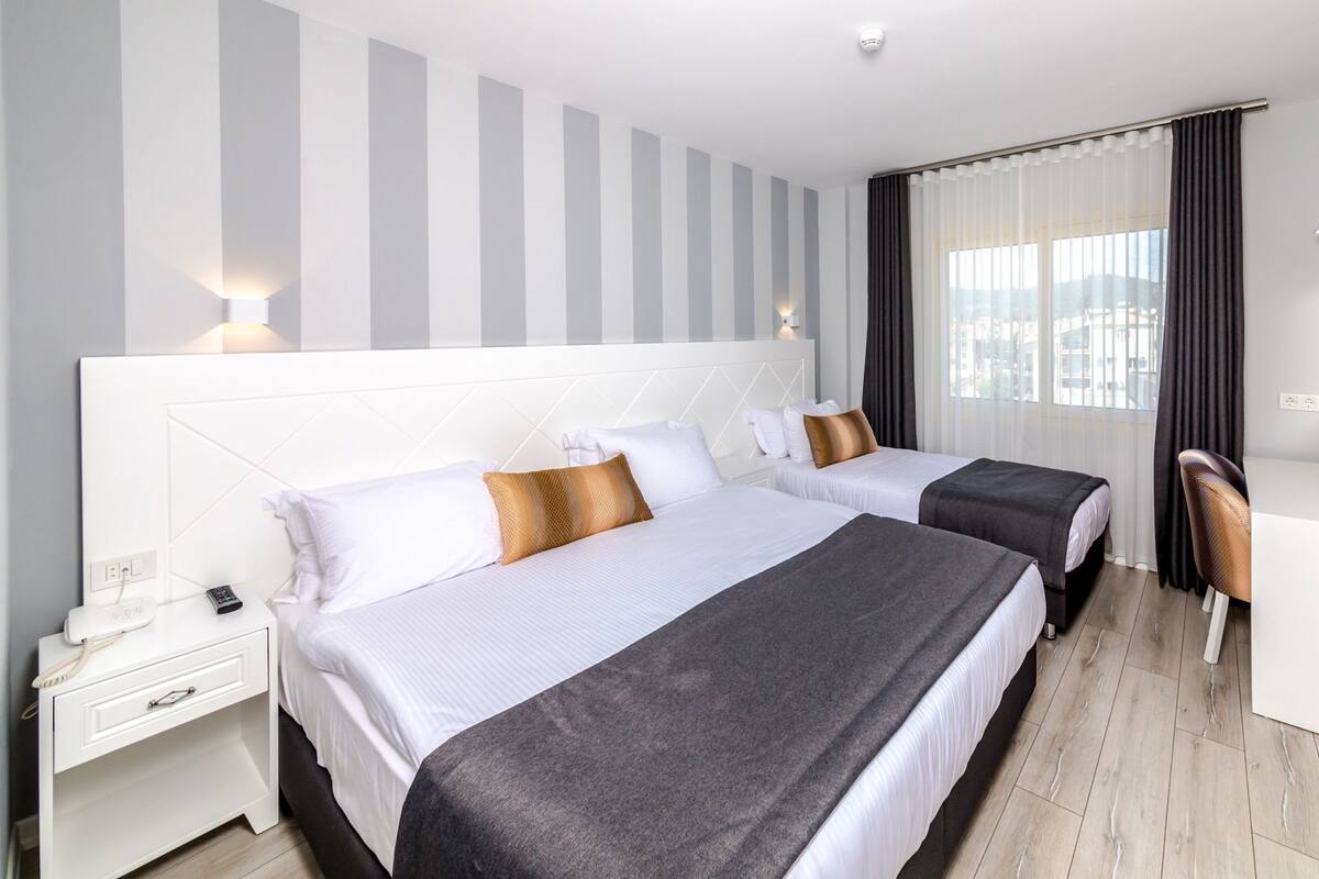 A hotel room with two beds, a desk, a chair, a TV, and a window with curtains.