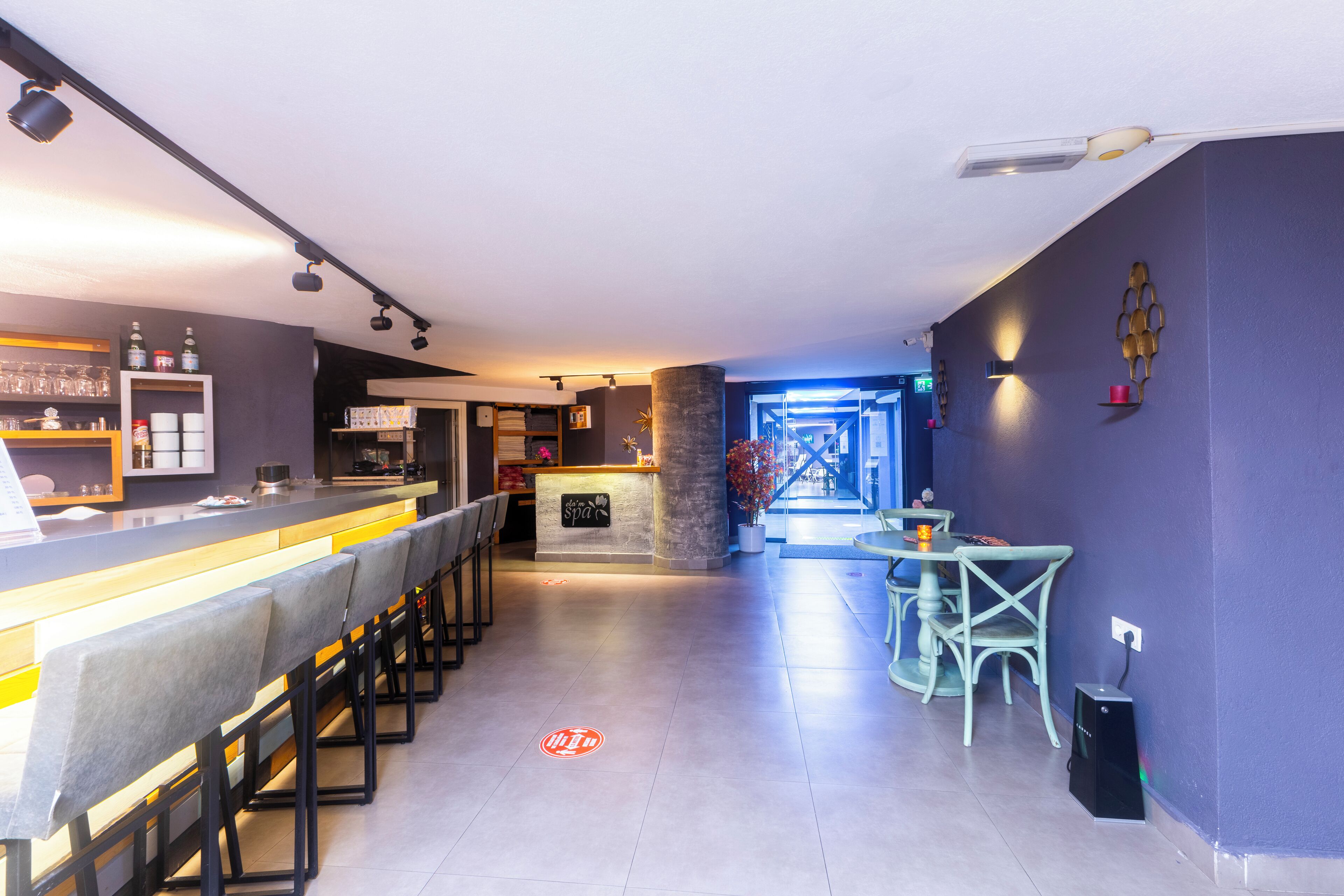 A modern bar area with a long counter, bar stools, and a seating area with chairs and a table.