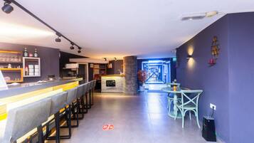 Uma área de bar moderna com um balcão comprido, banquetas e um espaço de estar com cadeiras e uma mesa.