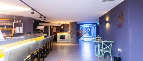 A modern bar area with a long counter, bar stools, and a seating area with chairs and a table.