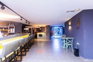 Uma área de bar moderna com um balcão comprido, banquetas e um espaço de estar com cadeiras e uma mesa.