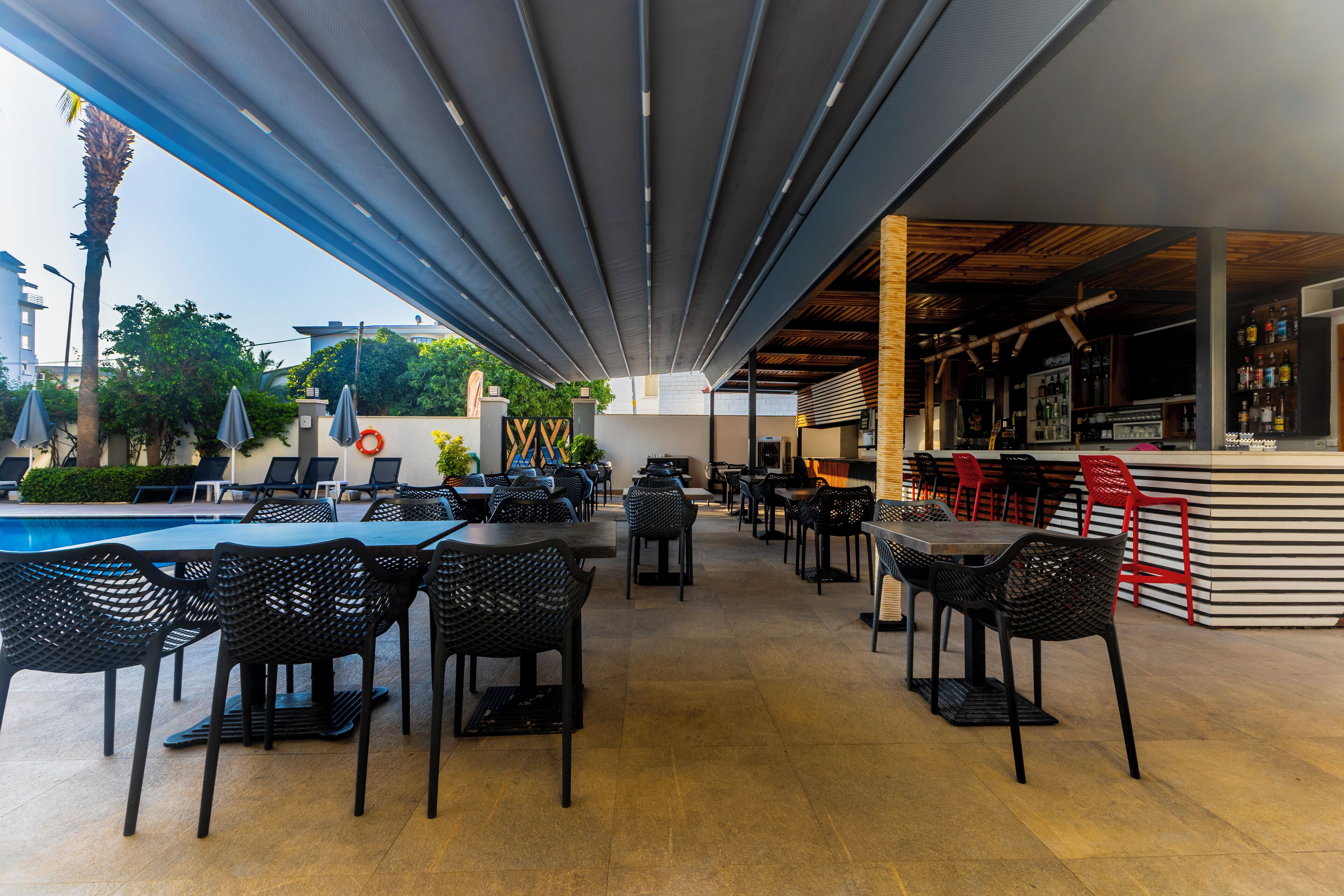 An outdoor cafe with tables and chairs, a pool, and a bar area.