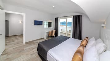 A hotel room with a large bed, a desk, a chair, a TV, and a balcony with a view.
