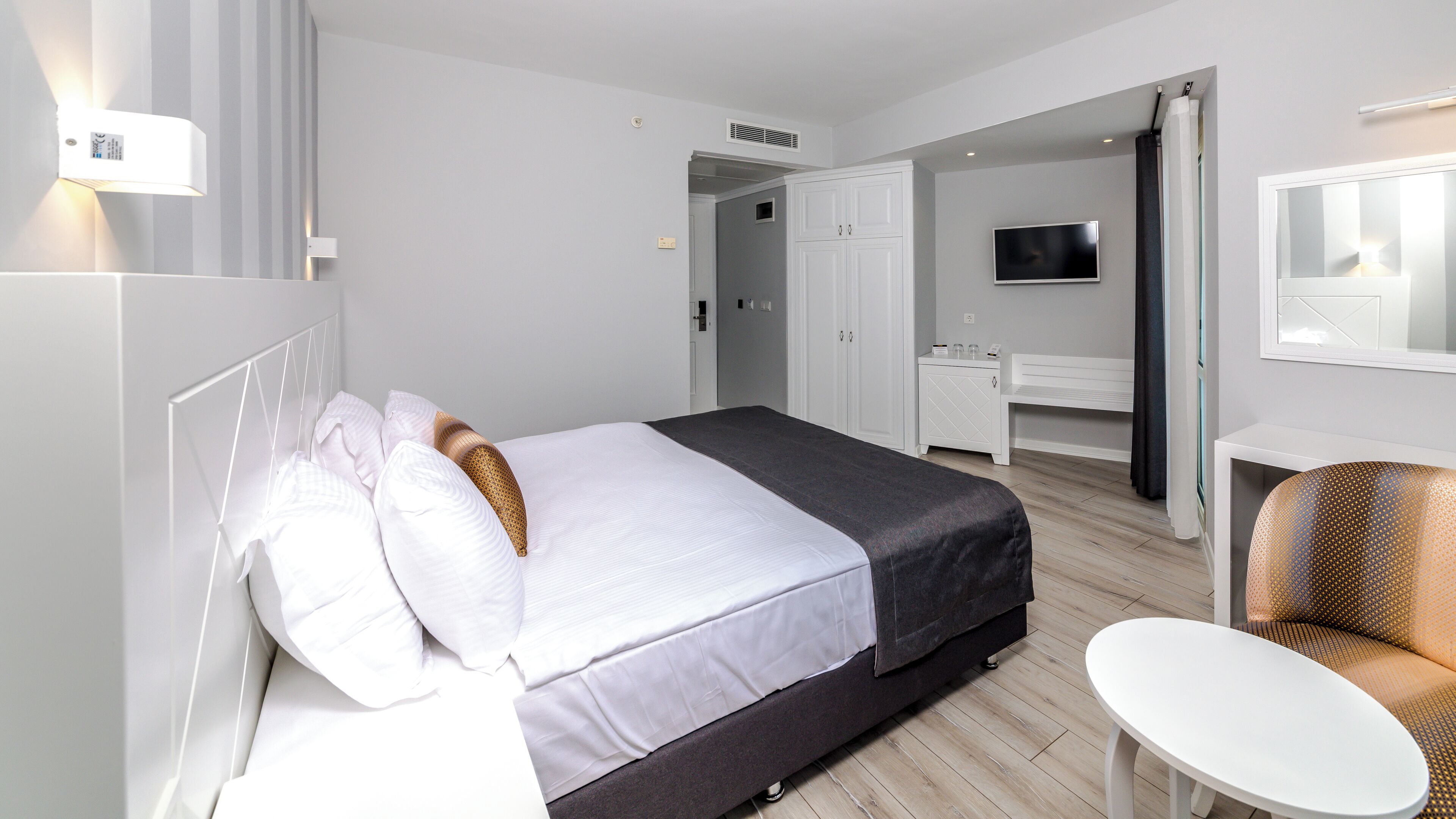 Quarto de hotel com cama, mesa de cabeceira, cadeira, televisão e guarda-roupa.