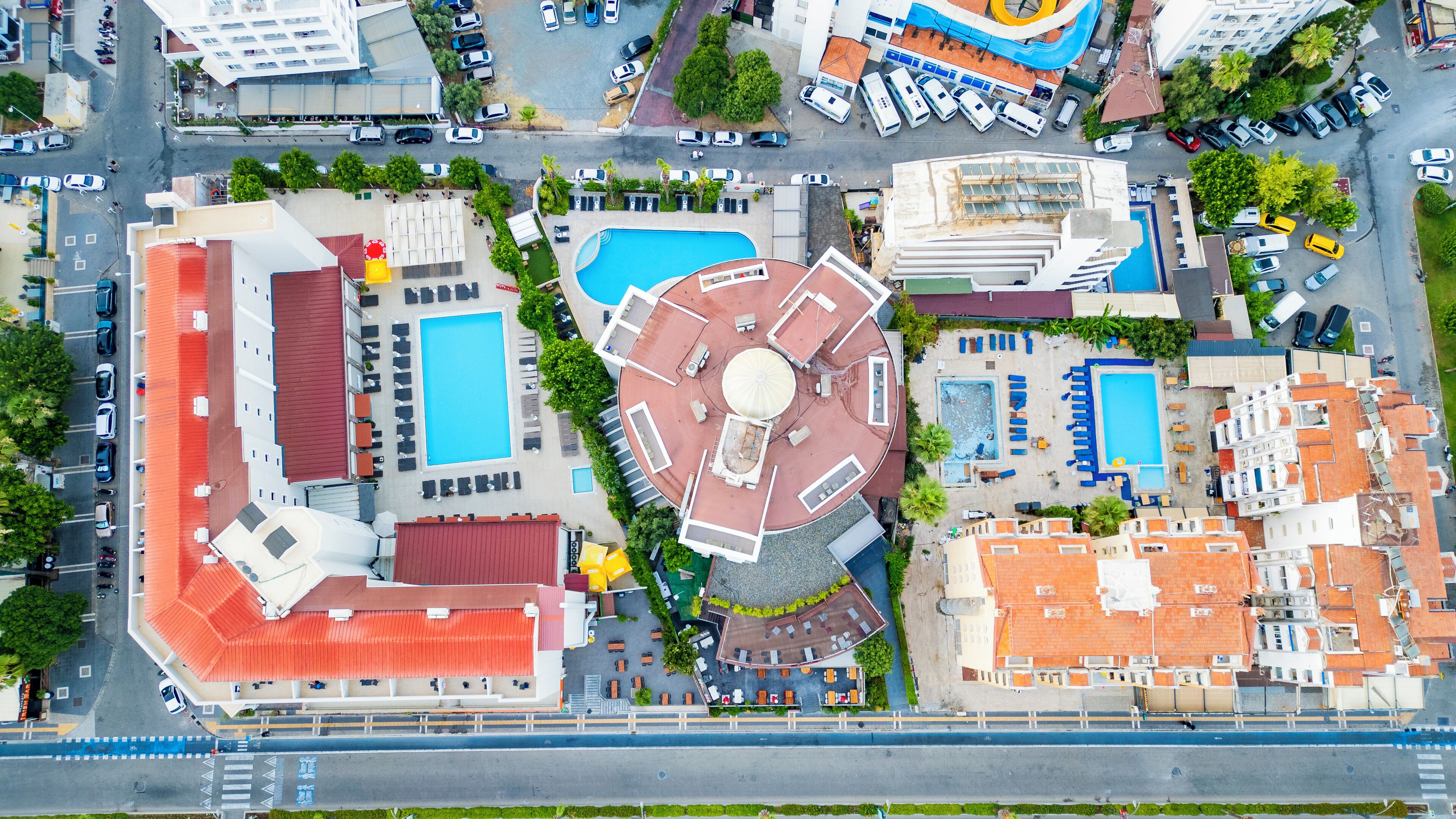 Vista aérea de un hotel con múltiples piscinas, un patio central y un estacionamiento.