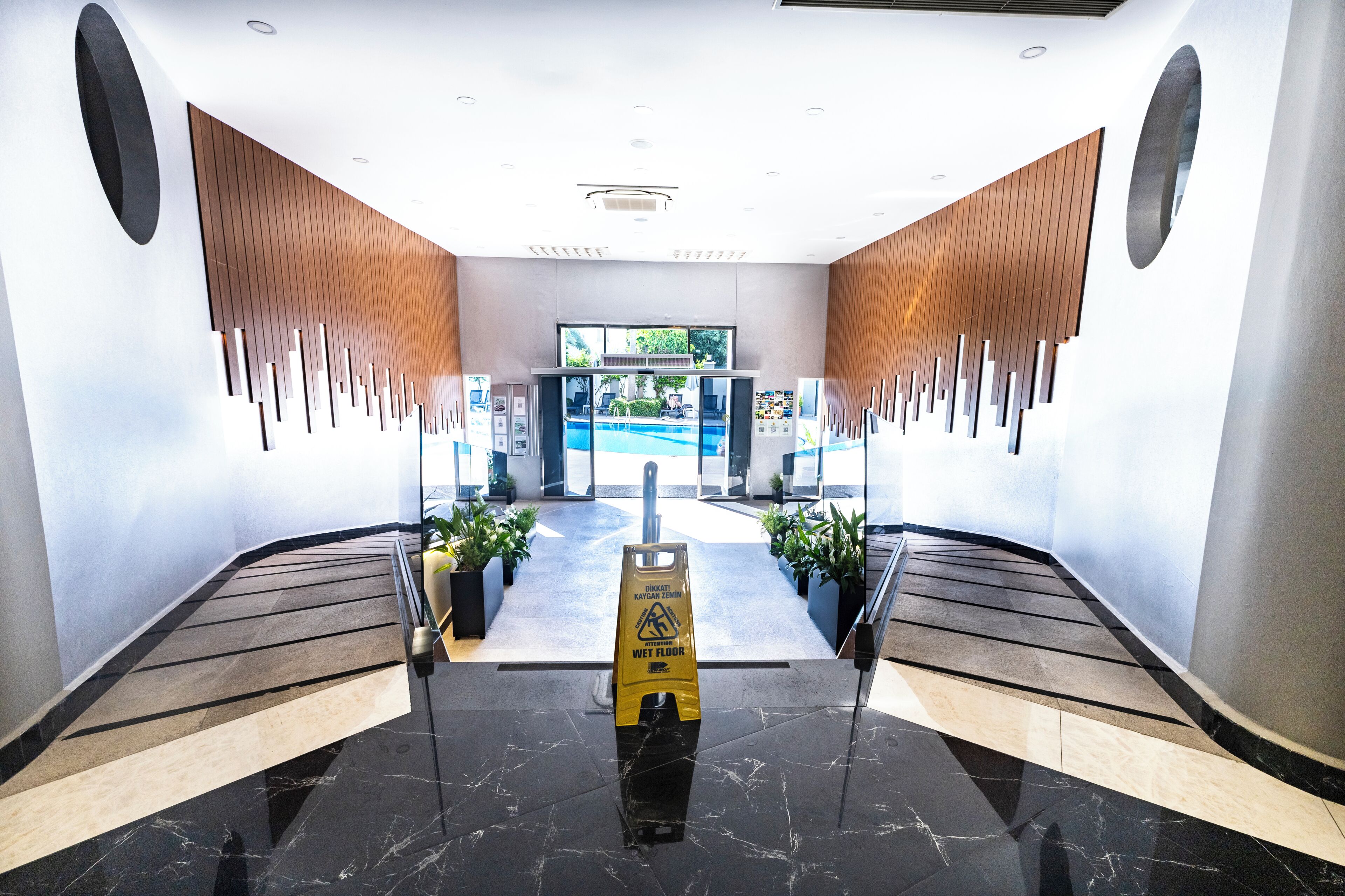 A modern lobby with a wet floor sign, a pool view, and a wooden slatted wall design.