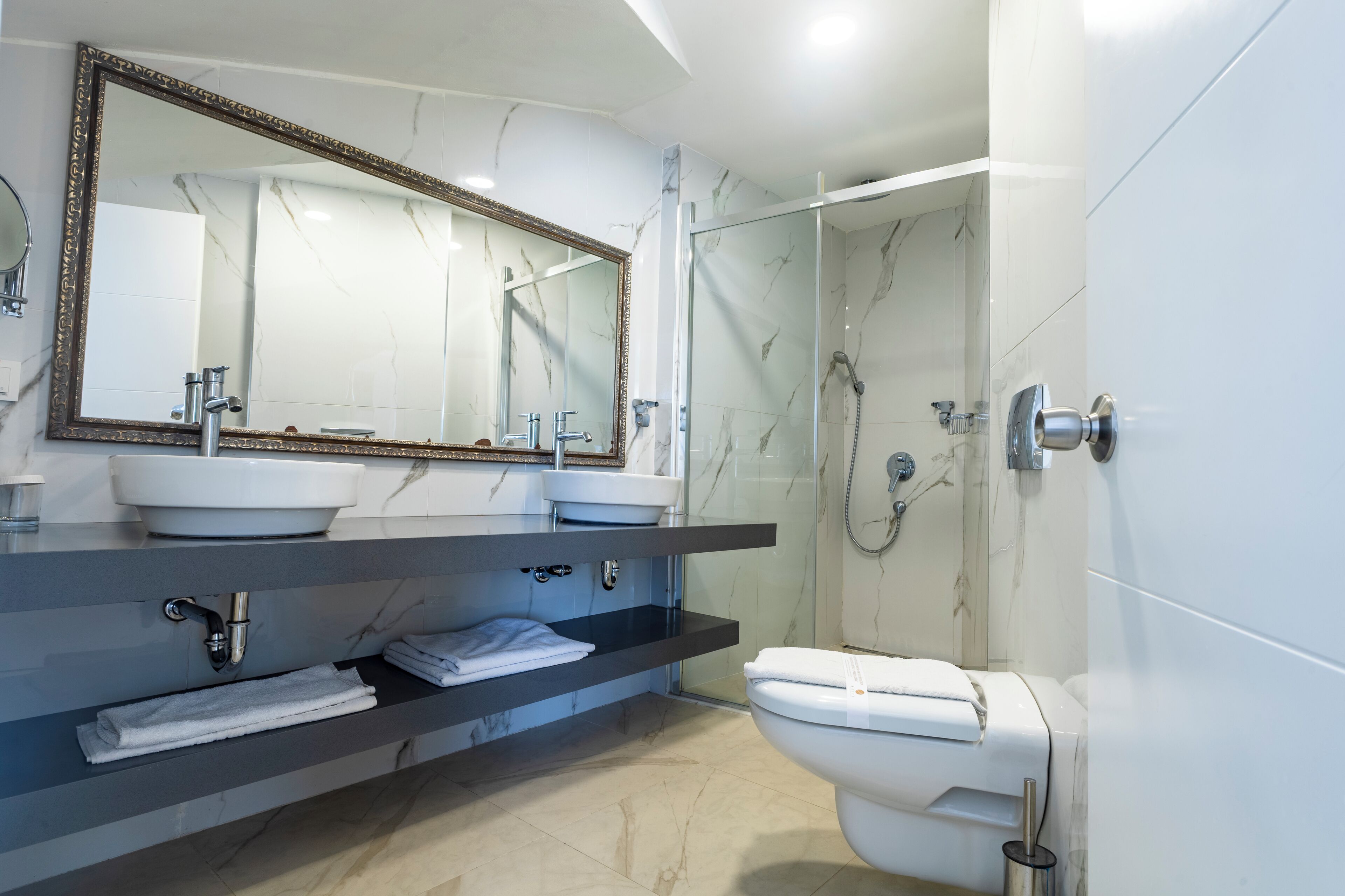 Un baño moderno con un espejo grande, dos lavamanos, inodoro y zona de ducha.