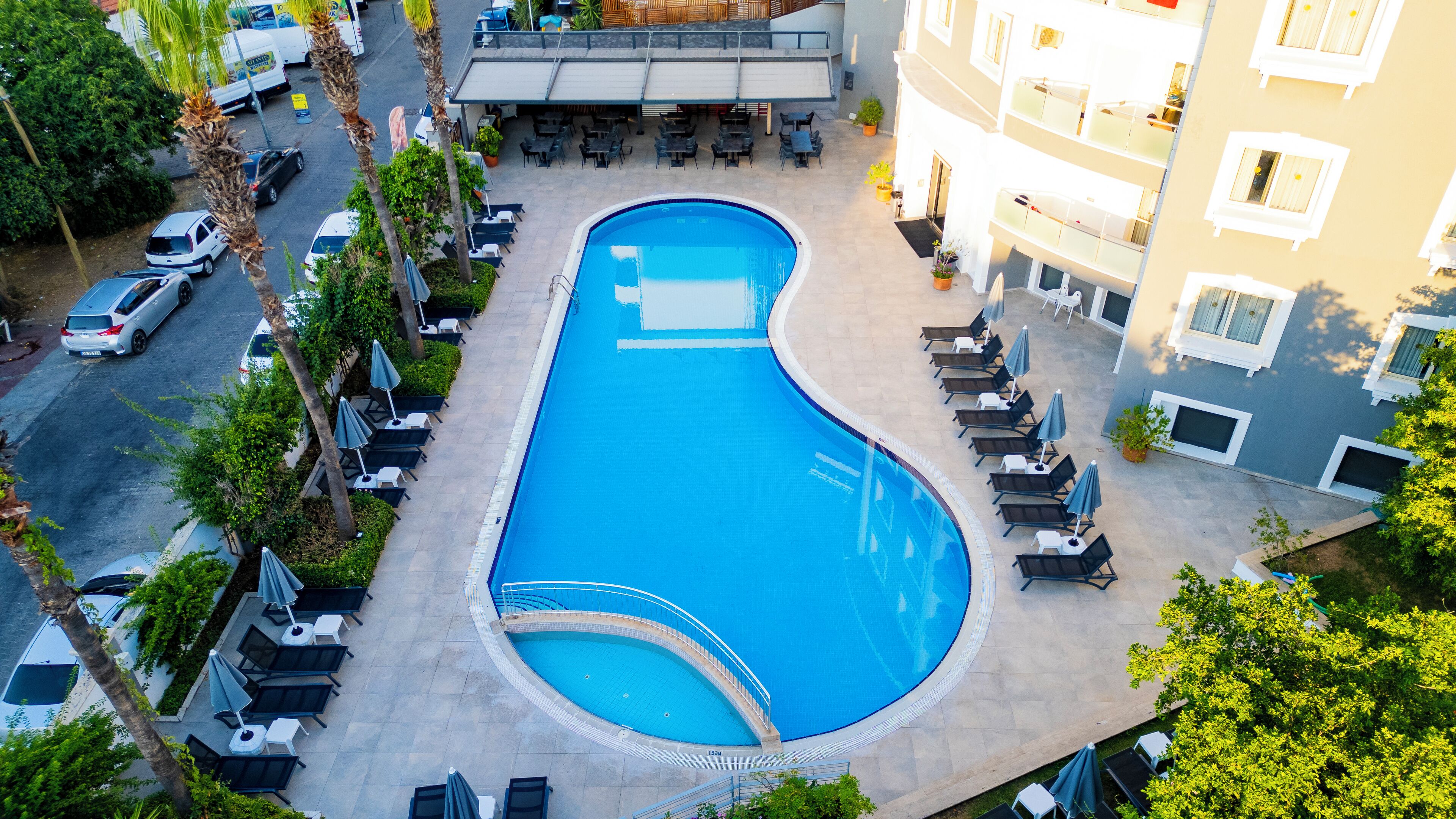 A swimming pool with lounge chairs and umbrellas, surrounded by a building with multiple floors and balconies.