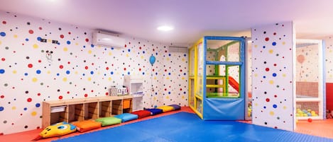 A playroom with colorful polka dot walls, a playpen, and a blue mat floor.