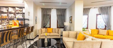 A modern living room with a bar area, two sofas, a dining table, and a chandelier.