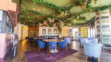 Un restaurante con una mesa redonda rodeada de sillas azules, una zona de bar con estanterías llenas de botellas y un techo decorado con plantas y luces colgantes.