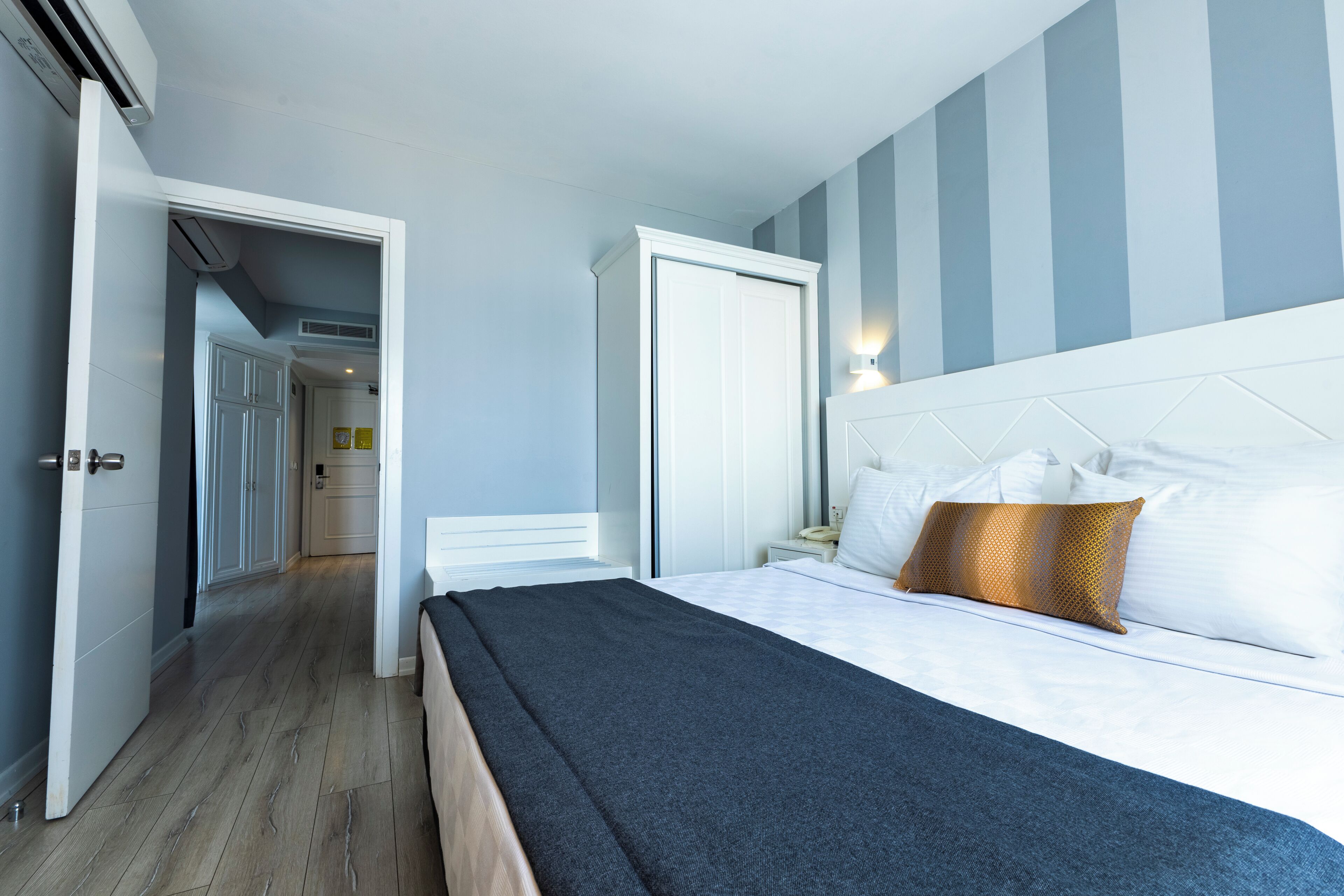 A hotel room with a bed, a nightstand, a wardrobe, and a hallway leading to another room.