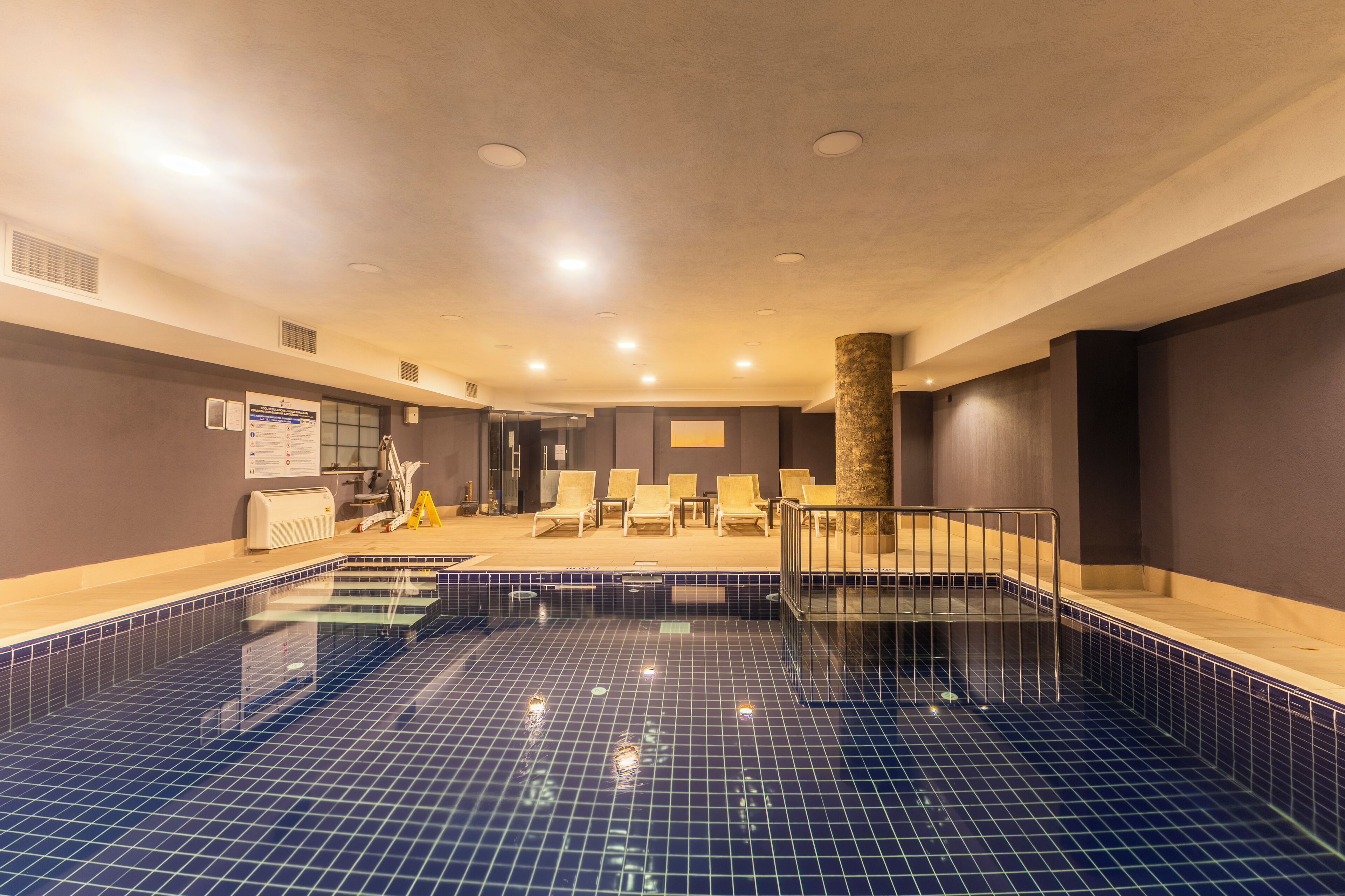 A swimming pool with a tiled floor and a sunken seating area with chairs.