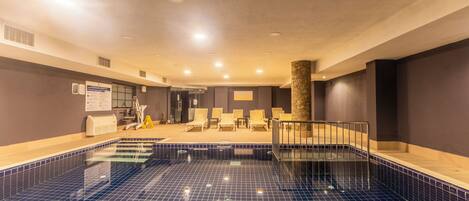 A swimming pool with a tiled floor and a sunken seating area with chairs.