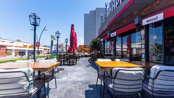 Un espace café en plein air avec des tables et des chaises, un parasol rouge et un bâtiment sur lequel on peut lire l’inscription « Happily ».