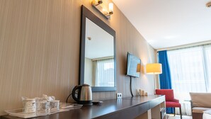 Habitación de hotel con un escritorio de madera oscura, un espejo grande, un televisor de pantalla plana, una silla roja y un sofá color beige.