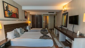 Una habitación de hotel con dos camas, un escritorio, un televisor y obras de arte en las paredes.