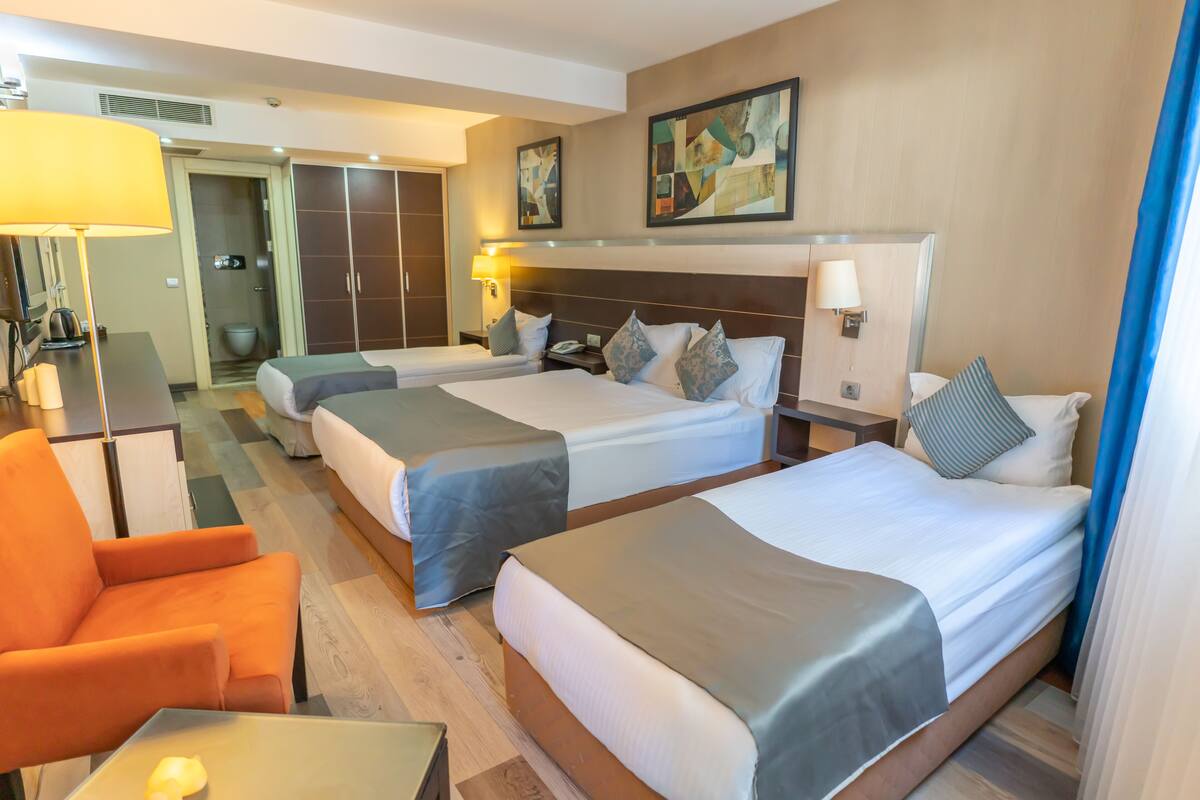 Une chambre d’hôtel avec deux lits, un bureau, une chaise et une salle de bain visible à travers une porte ouverte.