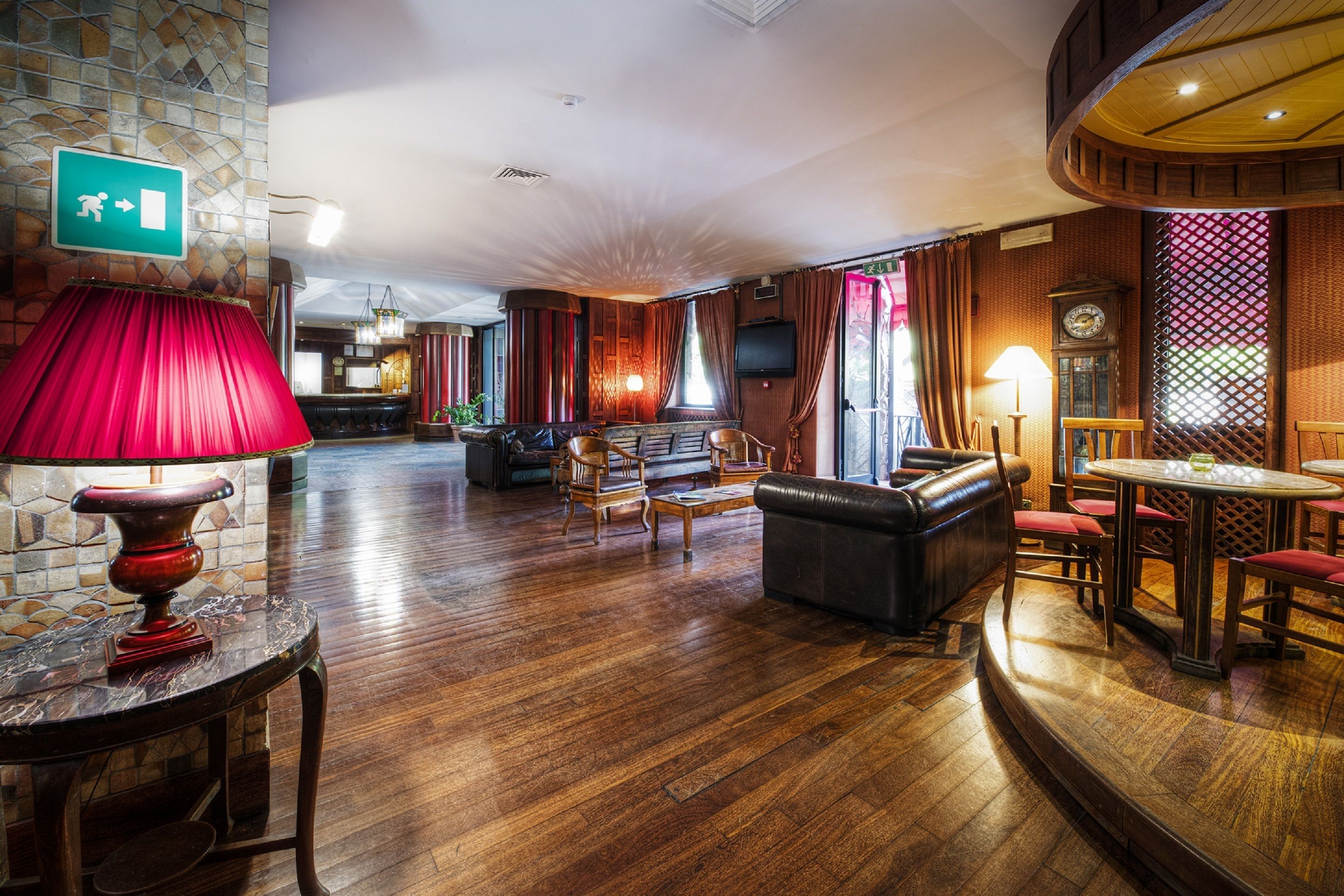 Un'ampia hall con pavimento in legno, zone relax, una lampada rossa e una sveglia.