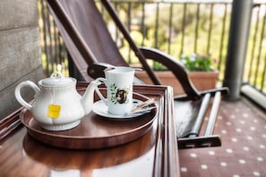 A tray with a teapot and a mug on a wooden table, set on a balcony with a railing and potted plants in the background. - Colony Hotel (Rome)