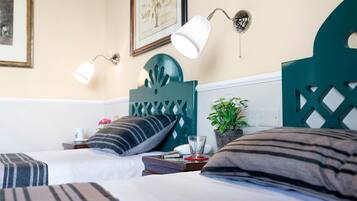 Camera d'albergo con due letti, una testiera, comodini, una lampada, una pianta e un quadro appeso al muro.