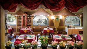 A restaurant with multiple tables, red tablecloths, and potted plants. - Colony Hotel (Rome)