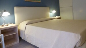 A hotel room with a bed, two bedside lamps, a nightstand, a chair, and a painting on the wall. - Hotel Da Cesare (Stresa)