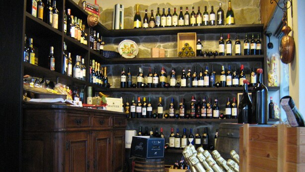 A wine cellar with numerous bottles on shelves and wooden barrels. - Hotel Da Cesare (Stresa)