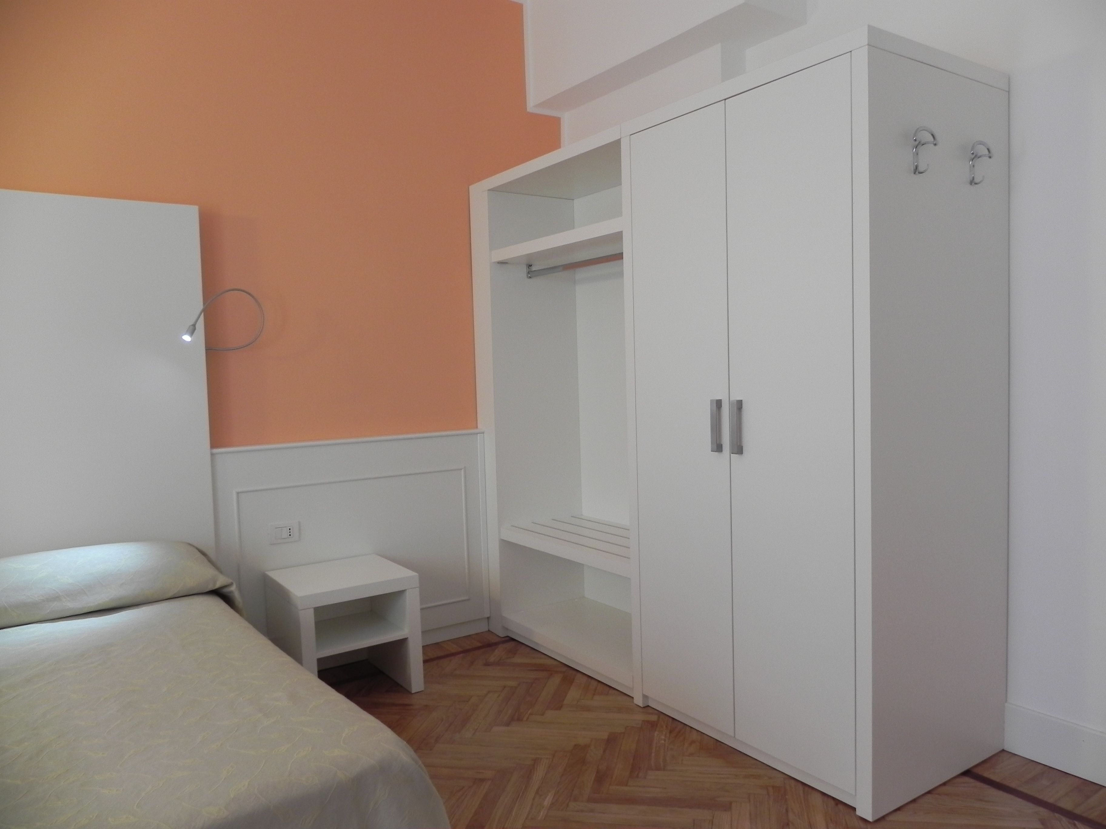A bedroom with a bed, a white wardrobe, and a small white nightstand.