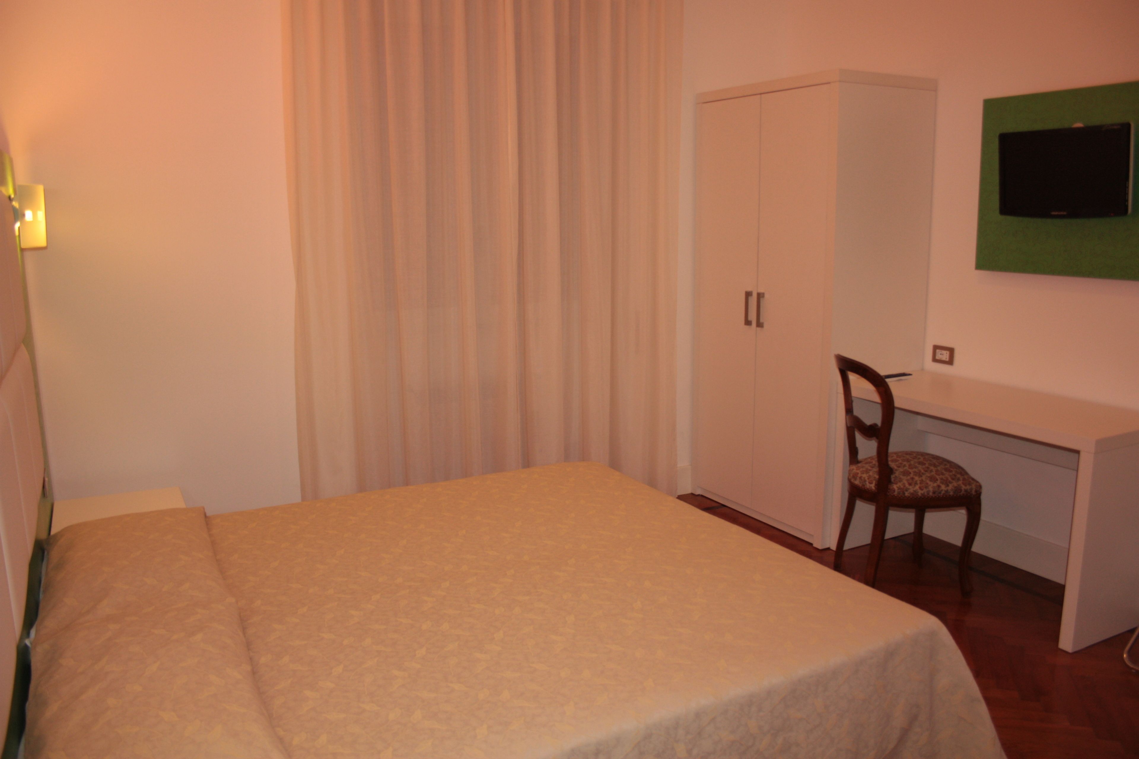 Ein Schlafzimmer mit Bett, Schreibtisch, Stuhl, Kleiderschrank und Fernseher an der Wand.
