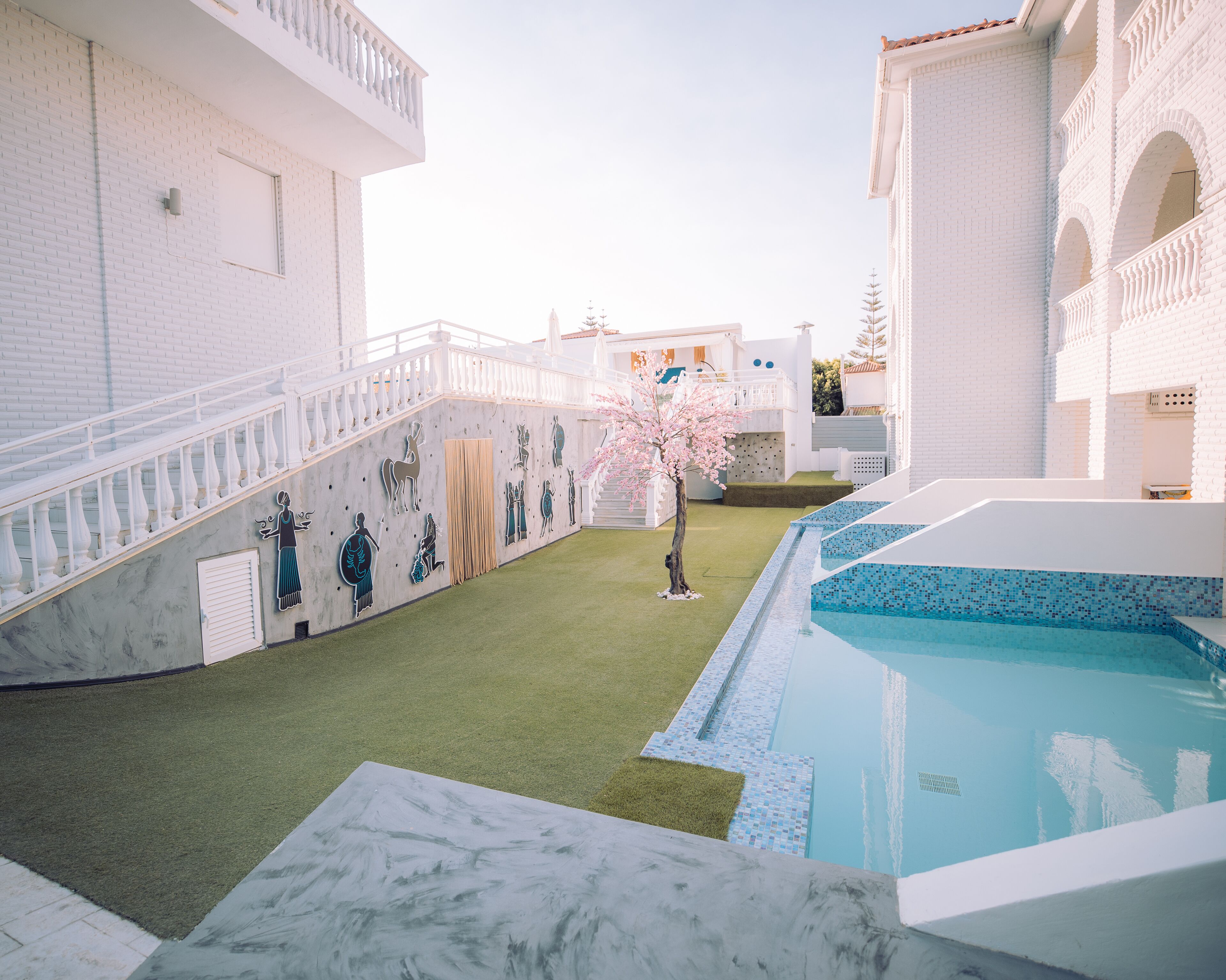 Un área de piscina con suelo de mármol, un pequeño jardín con césped artificial y una escalera con barandillas blancas.