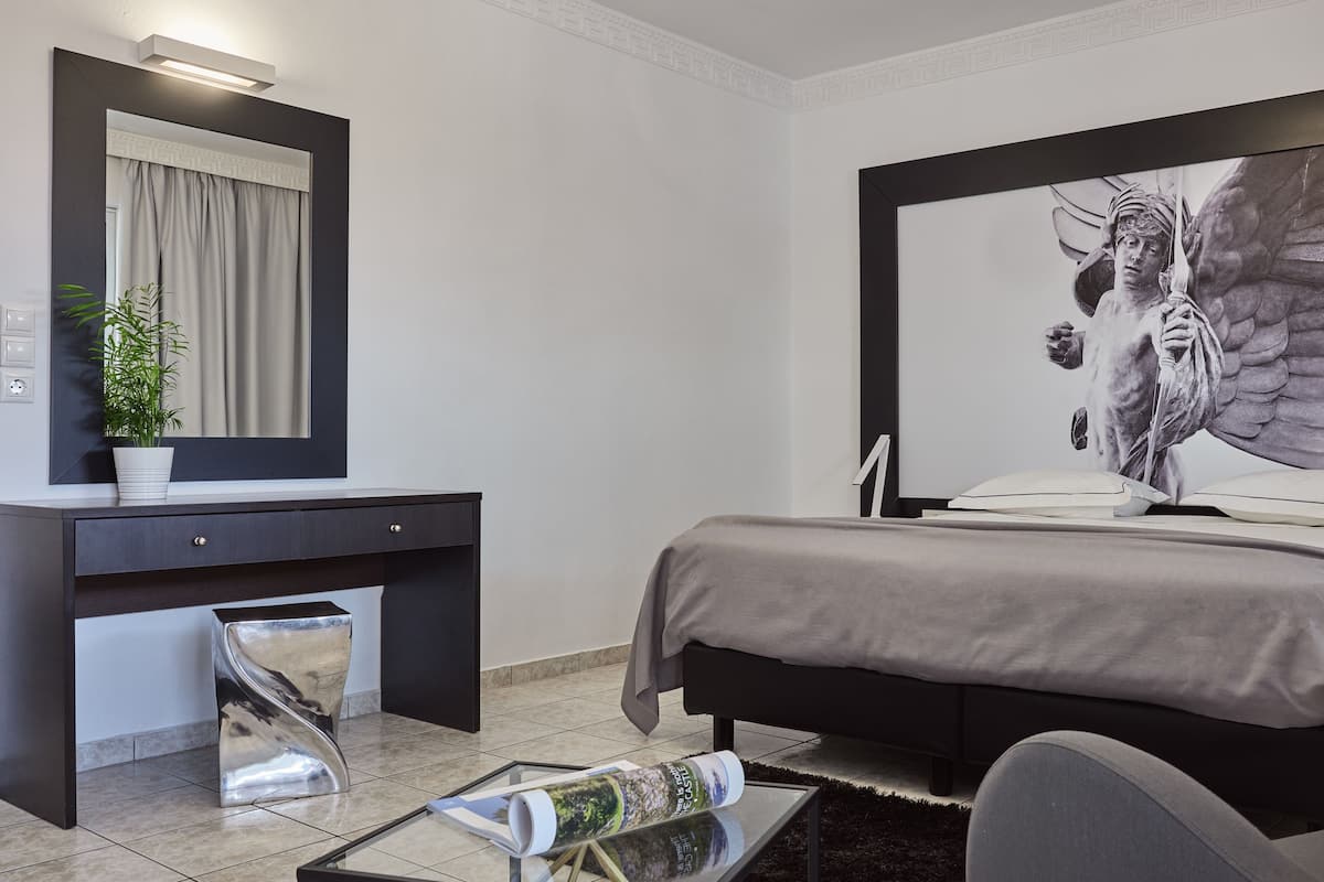Un dormitorio moderno con una cama grande, un aparador oscuro, un espejo y una obra de arte en la pared que representa una figura alada.