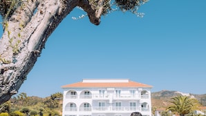 Une personne assise sur une couverture, sous un arbre, avec un bâtiment en arrière-plan.