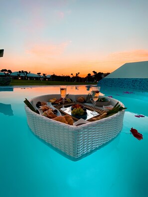 A floating dining setup with a basket of fruits and snacks, a glass of wine, and a bottle of water on a poolside. - Meandros Boutique & Spa Hotel - Adults Only (Zakynthos)
