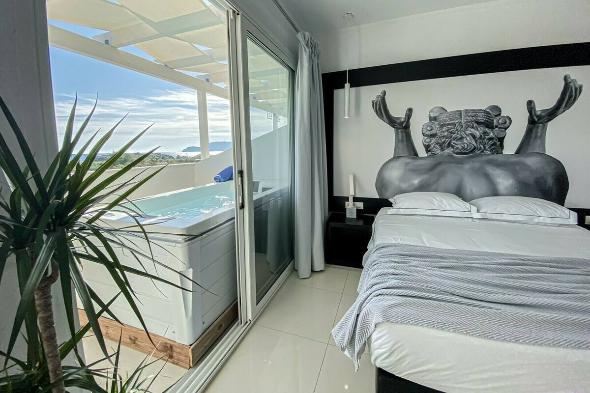 Una habitación de hotel moderna con una cama grande, vistas a una piscina y un balcón.