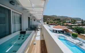 A balcony with a hot tub, a pool, and a view of a town with mountains in the background. - Meandros Boutique & Spa Hotel - Adults Only (Zakynthos)